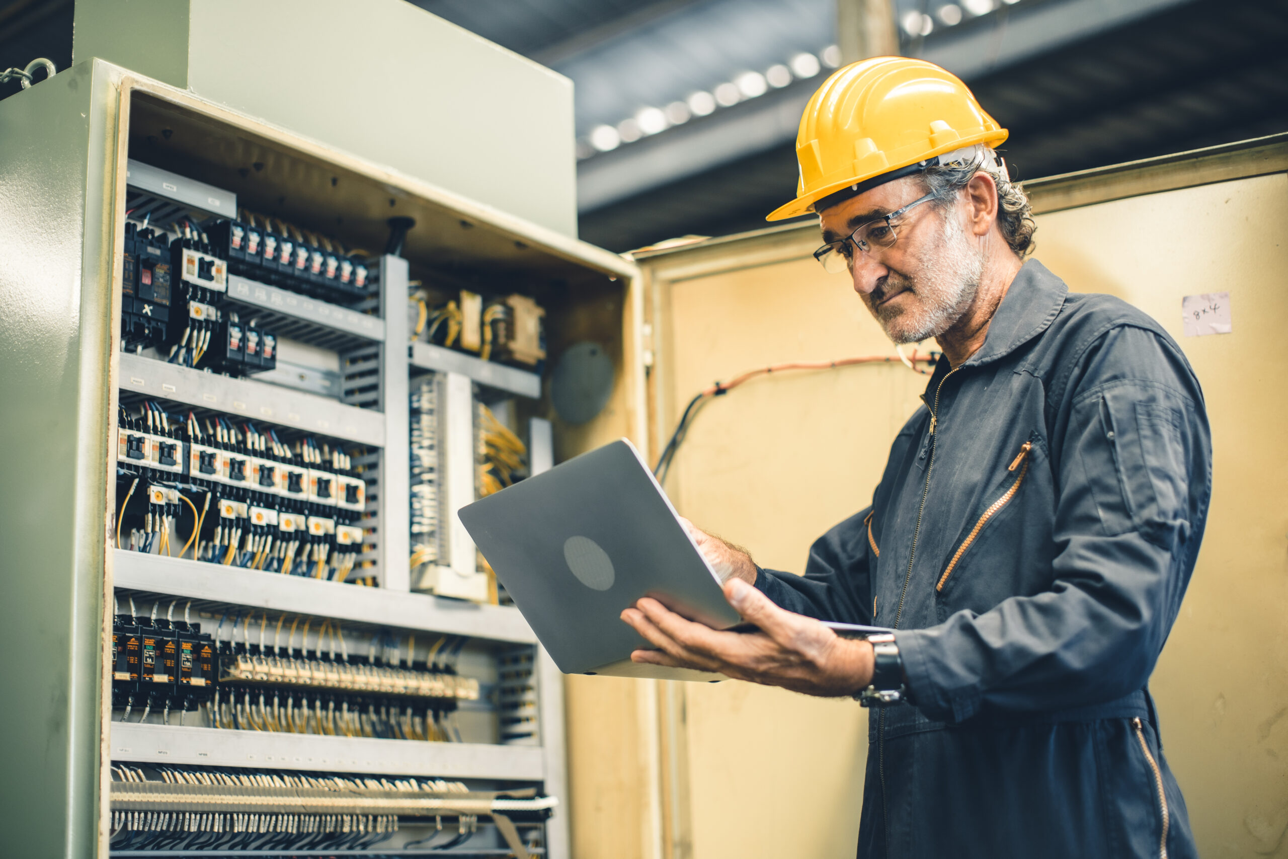 elektrische Industriemontage von TechCo - Arbeiter am Schaltschrank mit Laptop